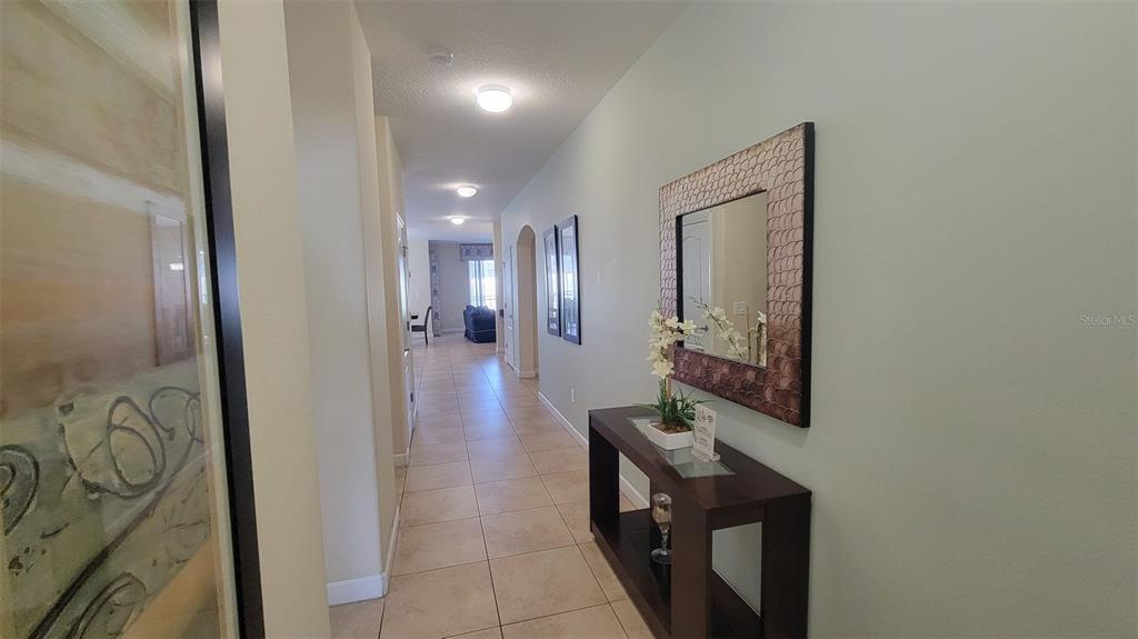 A hallway with tile flooring leads toward a living area, featuring a console table and mirror — 2952 BEACH PALM AVENUE, KISSIMMEE, FL
