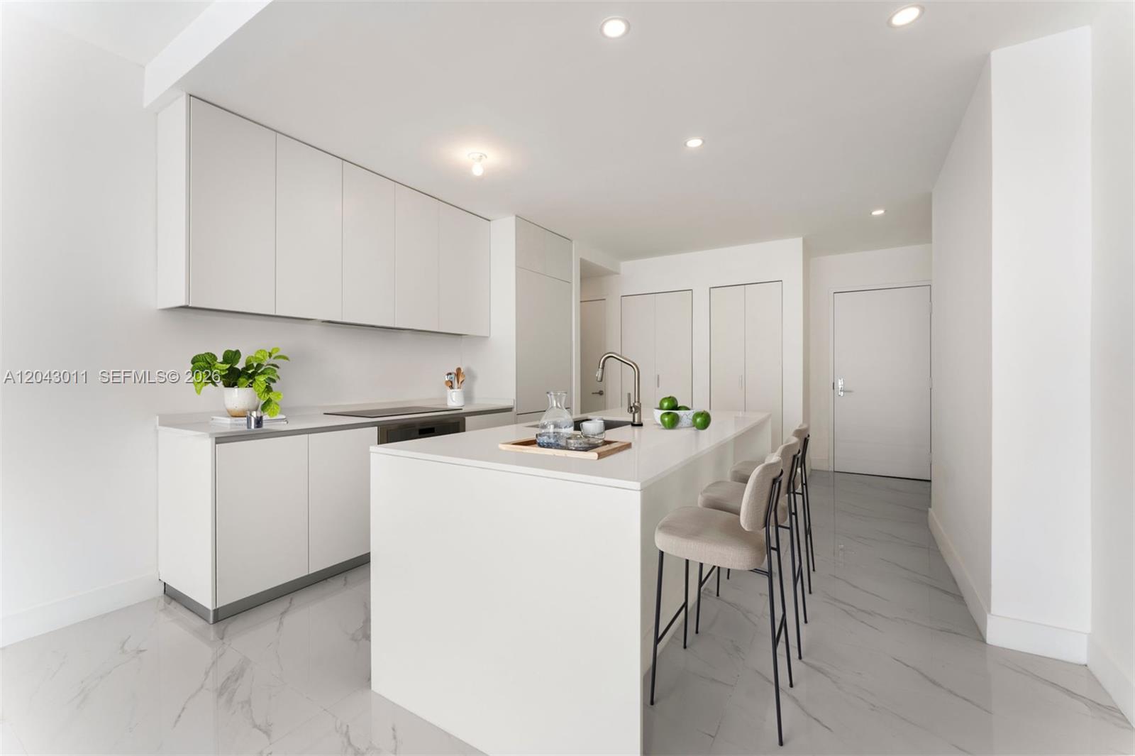 A modern white kitchen features a central island with bar stools and marble-look flooring — 700 NE 24 ST # 1004, Miami FL 33137, MIAMI, FL