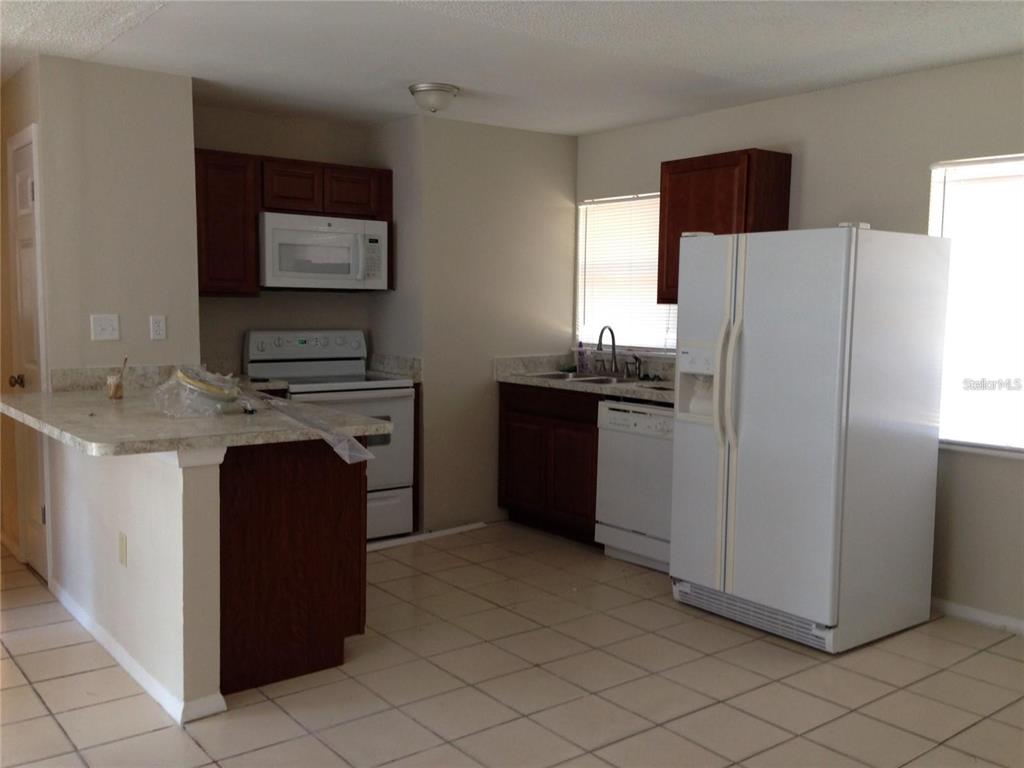 A kitchen features dark wood cabinets, white appliances, a breakfast bar, and light-colored tile flooring — 3650 TRIANON DRIVE, ORLANDO, FL