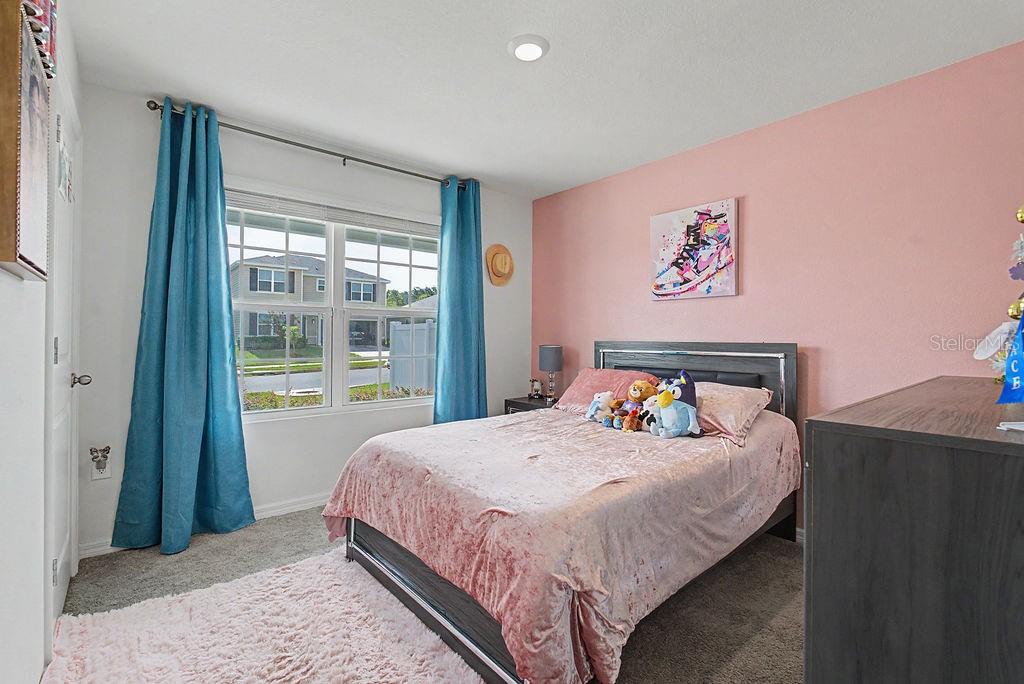 A bedroom features a pink accent wall, a bed with plush bedding, and blue curtains — 17070 NW 176TH WAY, ALACHUA, FL