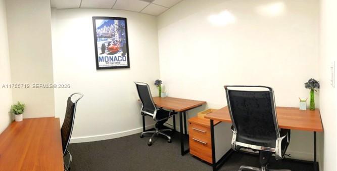A small office space features two wooden desks, black rolling chairs, and a Monaco poster — 150 SE 2nd Ave # 319, FL 33131, FL
