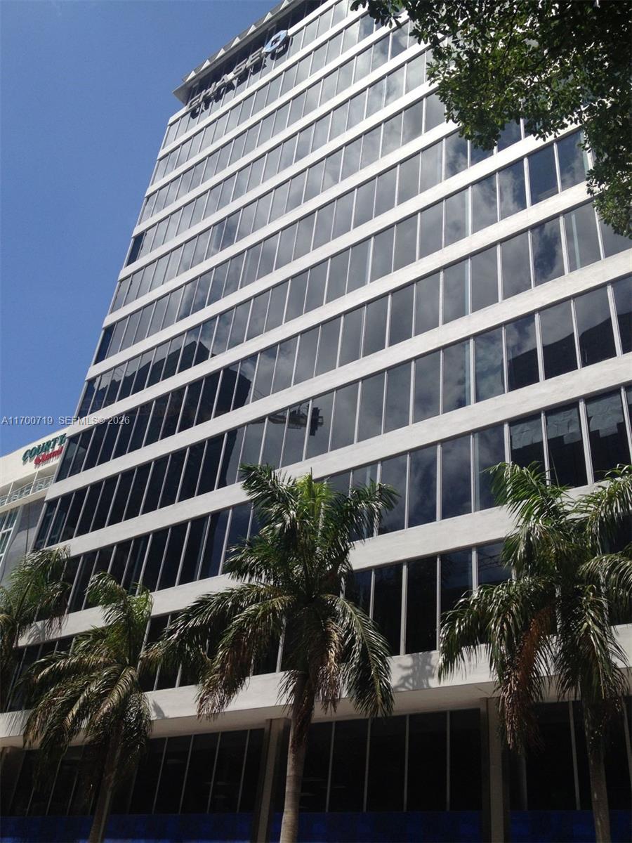 A low-angle exterior view of a multi-story office building with glass windows and palm trees — 150 SE 2nd Ave # 319, FL 33131, FL