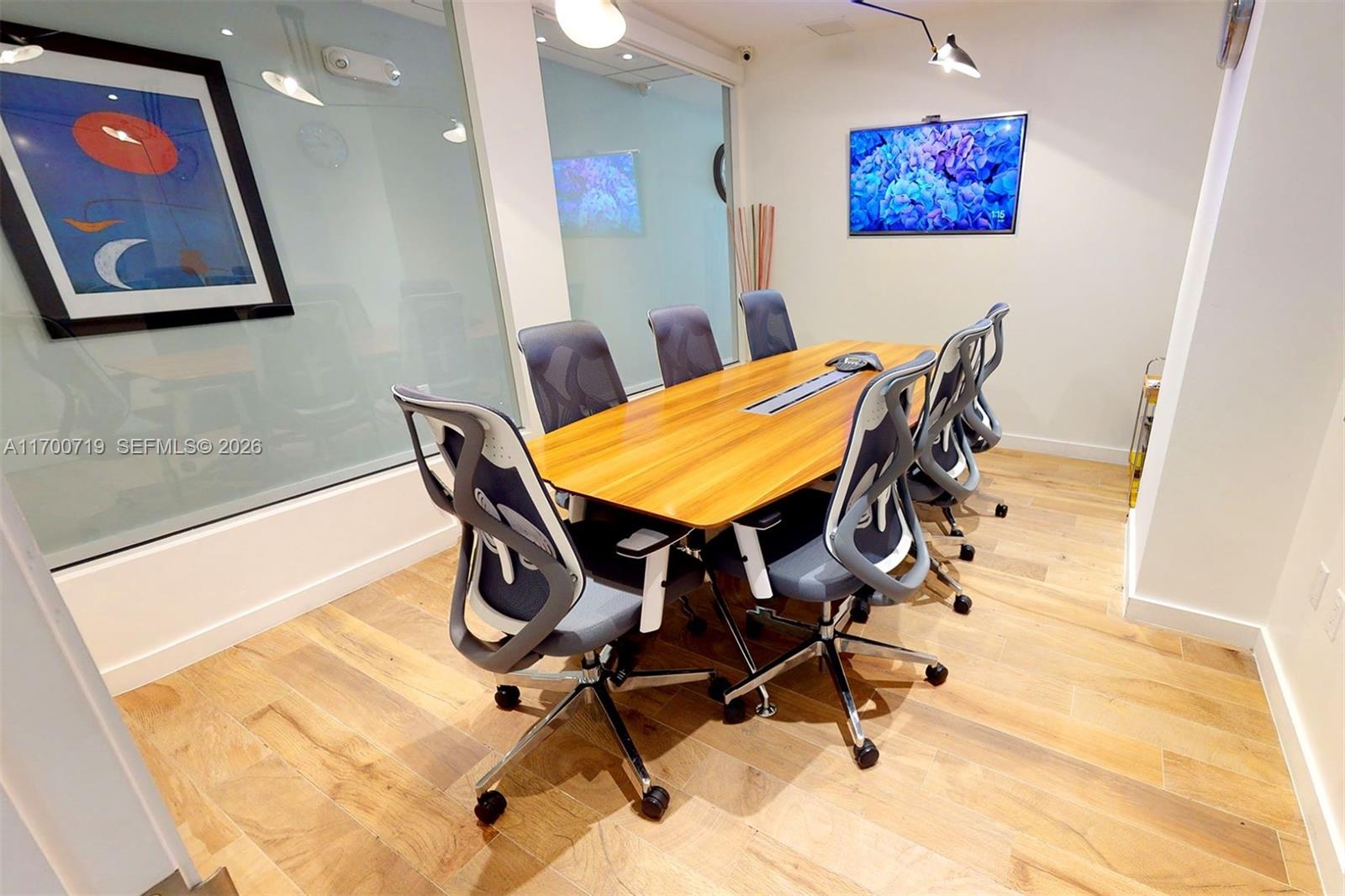 A modern conference room features a wooden table, gray ergonomic chairs, and wall-mounted artwork — 150 SE 2nd Ave # 319, FL 33131, FL