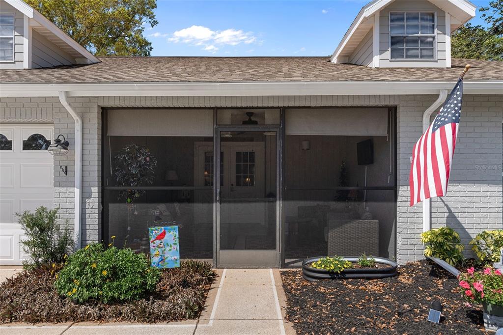 A screened-in front porch with a brick exterior and an American flag on the right — 2323 WESTCHESTER BOULEVARD, SPRING HILL, FL