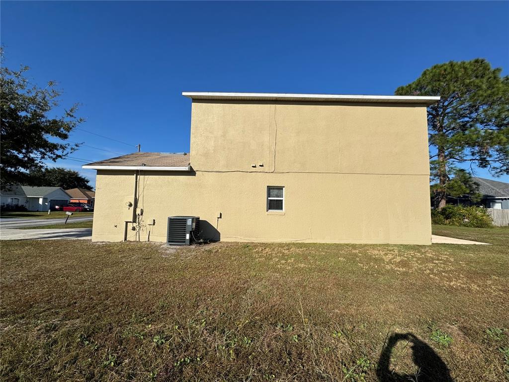A side view of a two-story tan stucco house with an exterior air conditioning unit — 681 BASINGSTOKE COURT, KISSIMMEE, FL