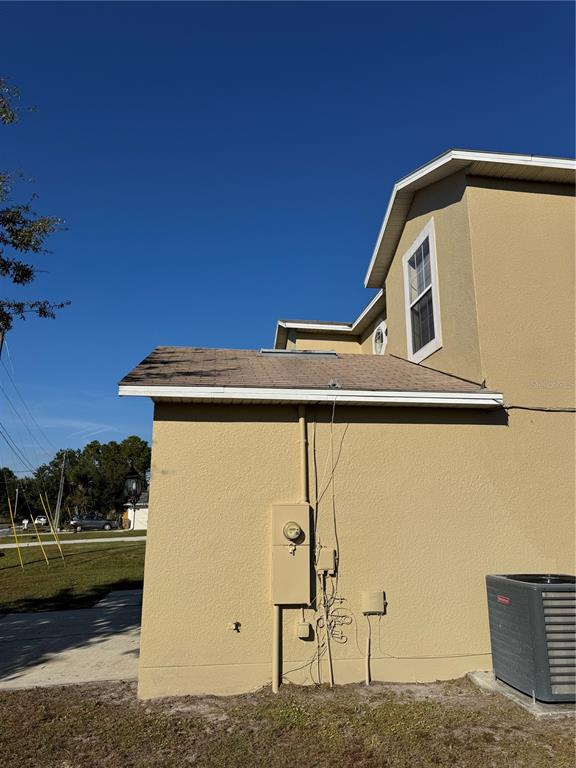 The exterior side view of a tan house shows a roof, utility meter, and HVAC unit — 681 BASINGSTOKE COURT, KISSIMMEE, FL