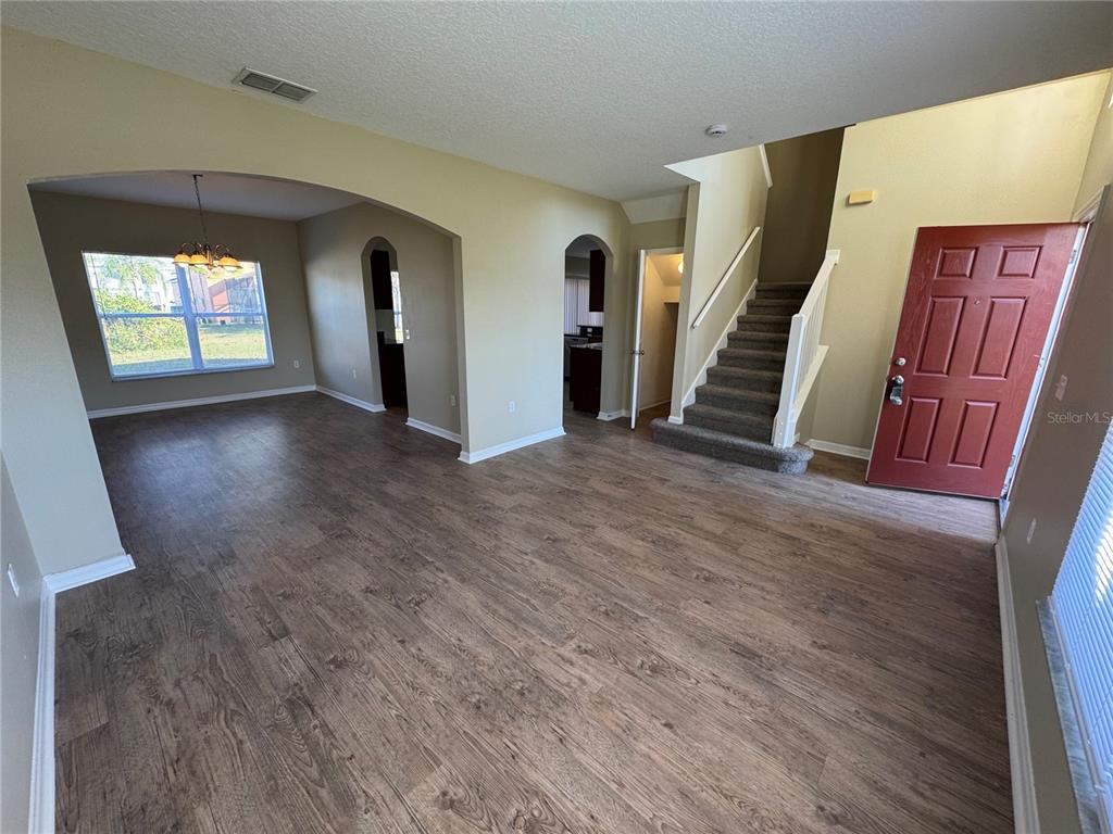 An open living area features wood-look flooring, a staircase, and a red front door — 681 BASINGSTOKE COURT, KISSIMMEE, FL