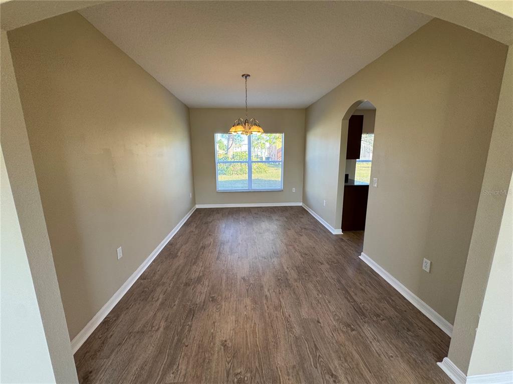 An empty dining room features wood-look flooring, beige walls, and a central chandelier — 681 BASINGSTOKE COURT, KISSIMMEE, FL