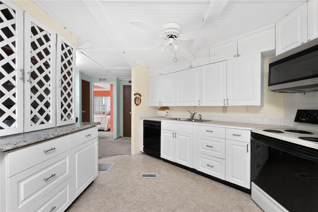 A kitchen features white cabinets, black appliances, a ceiling fan, and a view into another room — 1380 SEAGULL DRIVE, ENGLEWOOD, FL