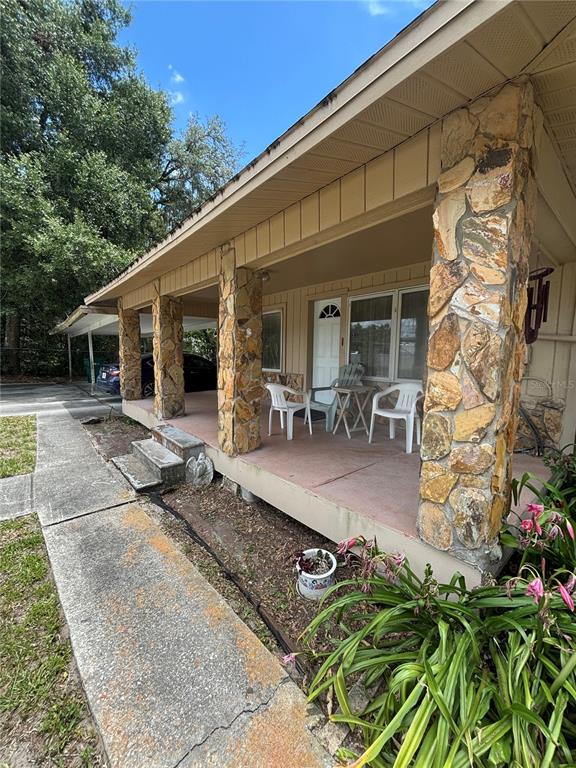 A covered front porch features stone-clad support columns, a concrete floor, and white plastic furniture — 13232 BLISSFIELD ROAD, ODESSA, FL