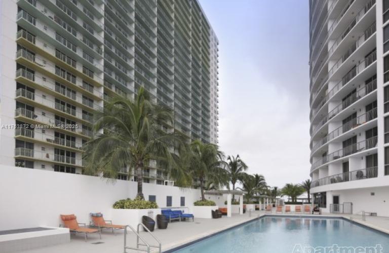 A swimming pool sits between two tall white residential buildings with balconies and palm trees — 1750 N Bayshore Dr # 2215, Miami FL 33132, MIAMI, FL