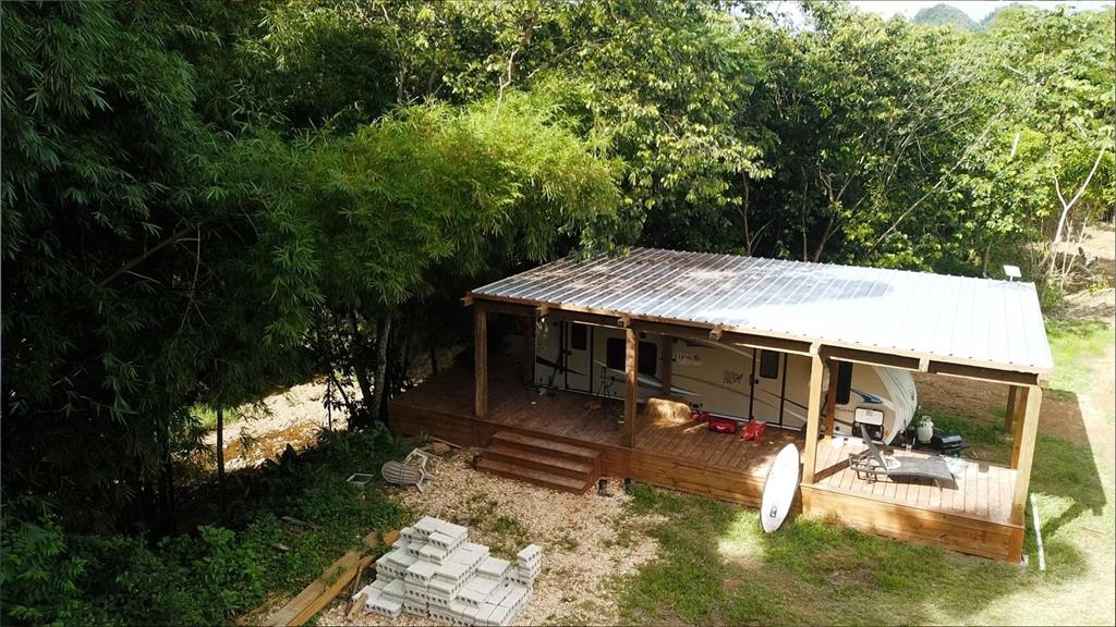 An aerial view shows a travel trailer parked under a wooden deck with a metal roof — 1 1  BO ANGELES, EL CORCHO, UTUADO, PR