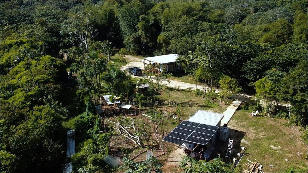 An aerial view shows a rural property with a house, solar panels, and surrounding forest — 1 1  BO ANGELES, EL CORCHO, UTUADO, PR