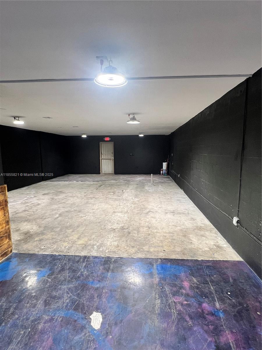 An empty industrial-style room features black walls, concrete flooring, and overhead pendant lighting — 1657 W 40th St # 6, Hialeah FL 33012, HIALEAH, FL