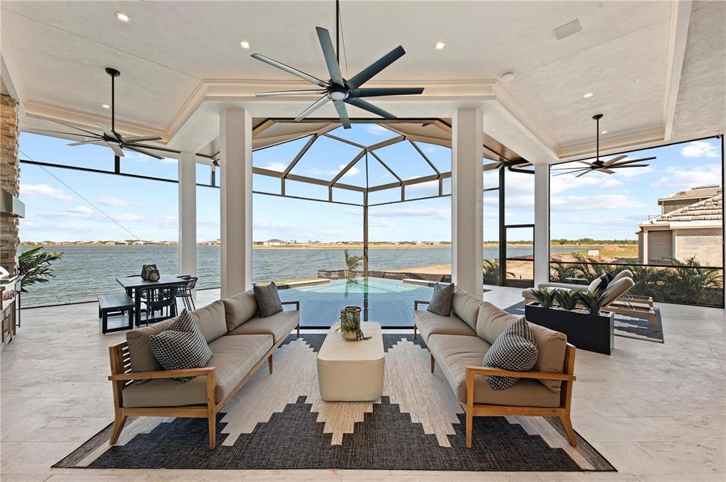 A covered outdoor patio features two sofas, a pool, and a view of a lake — 800 BLUE SHELL LOOP, SARASOTA, FL
