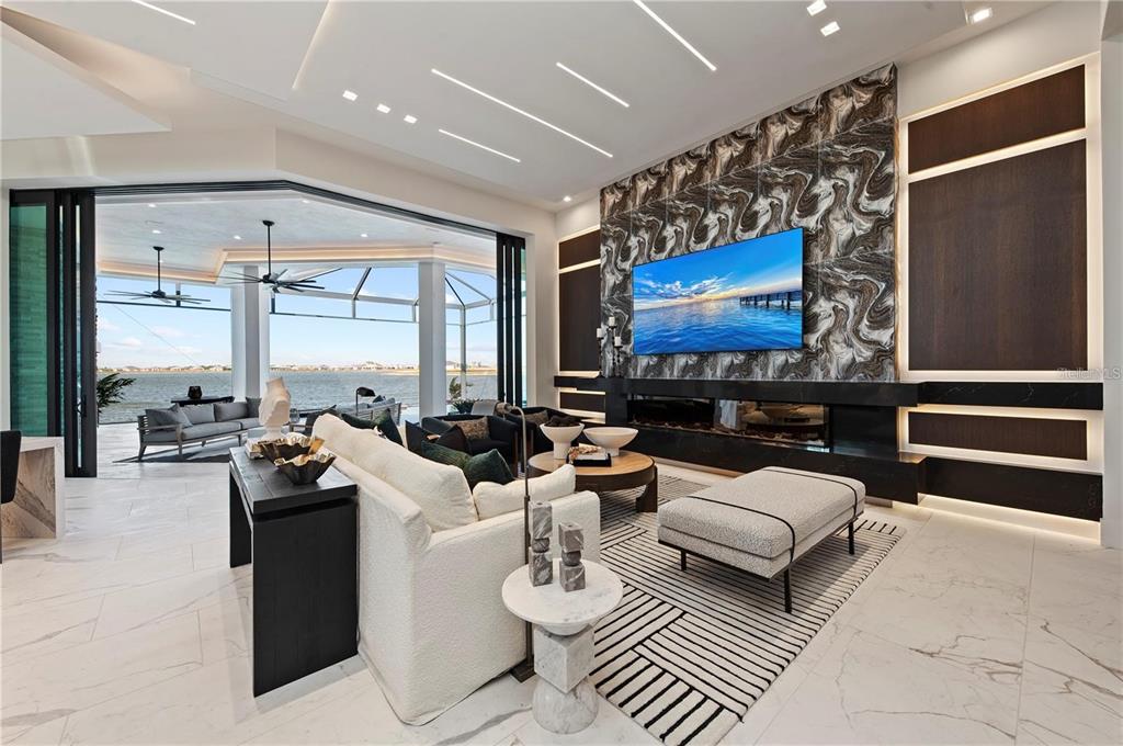 A modern living room features a marble fireplace wall, large sliding glass doors, and water views — 800 BLUE SHELL LOOP, SARASOTA, FL