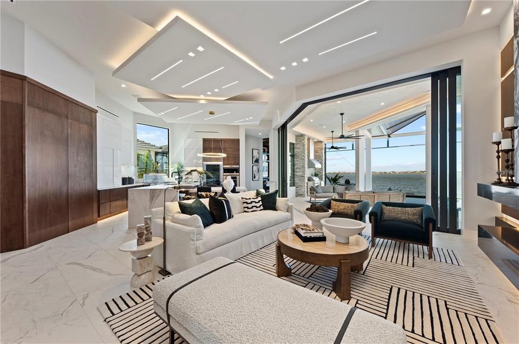 A modern open-concept living room features a tiered tray ceiling, marble floors, and waterfront views — 800 BLUE SHELL LOOP, SARASOTA, FL