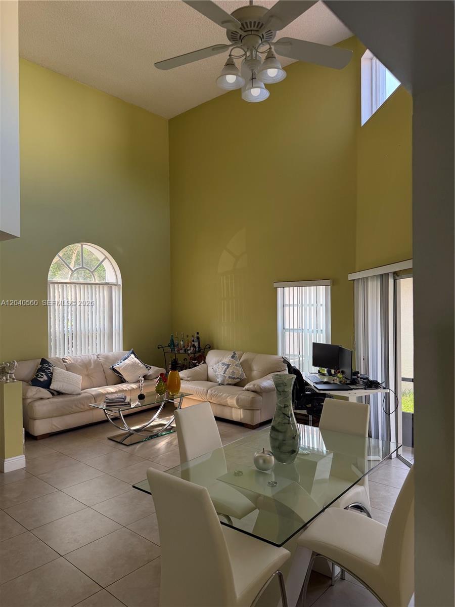 A high-ceilinged living and dining area features tile floors, beige sofas, and a glass table — 1335 Seagrape Cir, Weston FL 33326, WESTON, FL