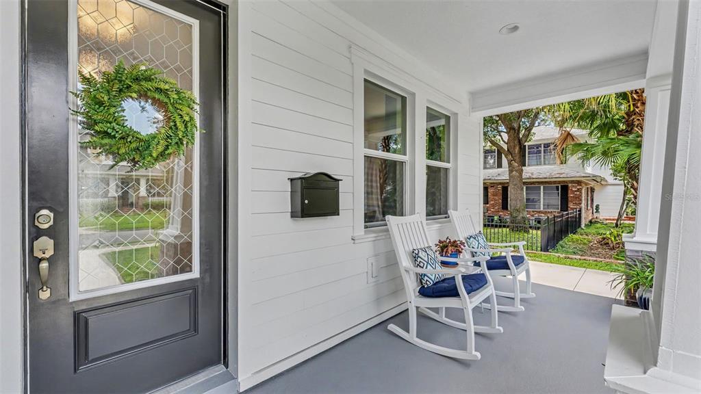 A covered front porch features white siding, a black door, and two white rocking chairs — 1829 CHEROKEE TRAIL, LAKELAND, FL