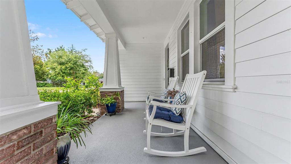 A covered front porch features white siding, brick columns, and two white rocking chairs — 1829 CHEROKEE TRAIL, LAKELAND, FL
