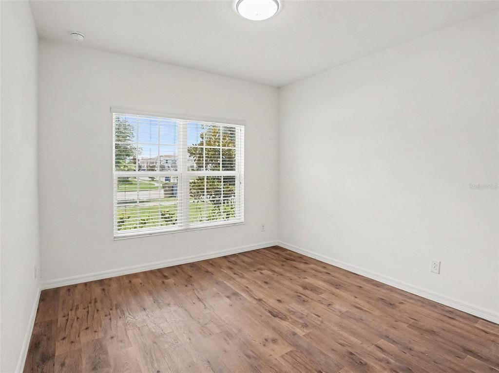 An empty bedroom features white walls, wood-look flooring, and a window with white blinds — 5583 SABAL DRIVE, ST CLOUD, FL