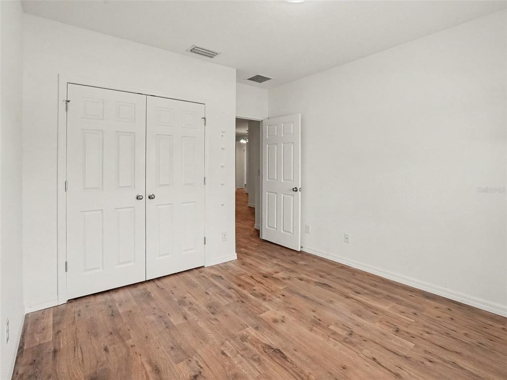 An empty bedroom with white walls, wood-look flooring, a double-door closet, and an open doorway — 5583 SABAL DRIVE, ST CLOUD, FL