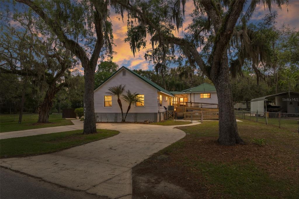 A white house with a green metal roof sits behind a concrete driveway and trees — 5447 S BOULEVARD DRIVE, HOMOSASSA, FL