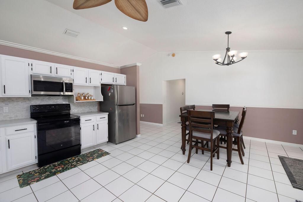 A kitchen with white cabinets, stainless steel appliances, and a dining table on tiled floors — 14502 69th Street N, FL 33470, FL