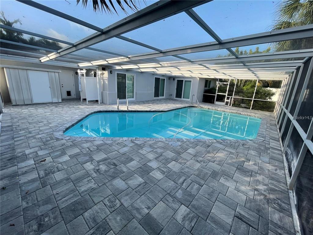 A screened-in patio features a swimming pool surrounded by gray stone pavers — 2460 E VINA DEL MAR BOULEVARD, ST PETE BEACH, FL