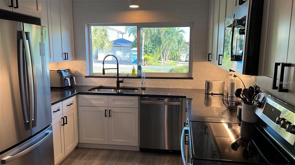 A kitchen features white cabinets, dark countertops, stainless steel appliances, and a window above the sink — 2460 E VINA DEL MAR BOULEVARD, ST PETE BEACH, FL