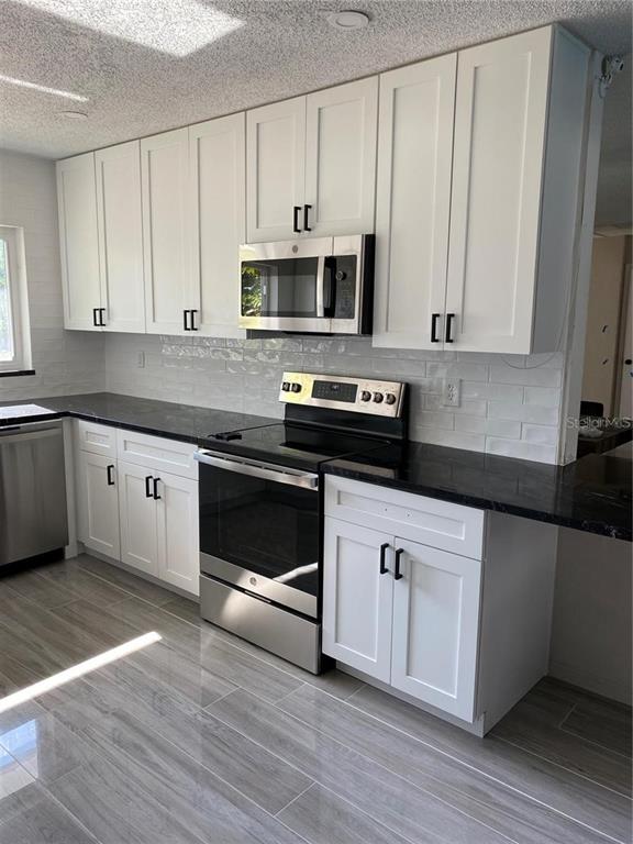 A kitchen features white cabinets, black countertops, stainless steel appliances, and gray wood-look tile flooring — 2460 E VINA DEL MAR BOULEVARD, ST PETE BEACH, FL