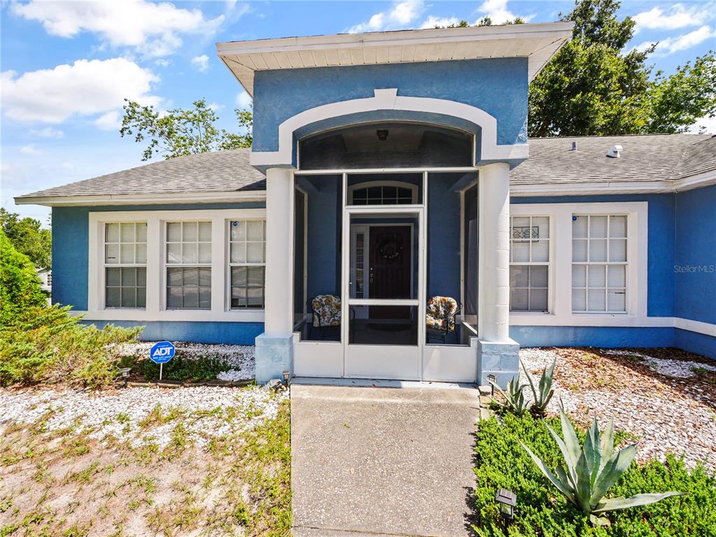 The exterior of a blue house features a screened-in front porch with two chairs — 3244 FIELDCREST TERRACE, DELTONA, FL