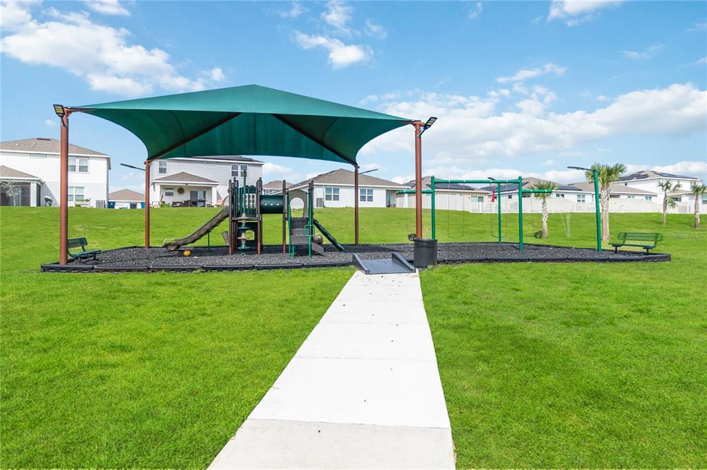 A playground with a green shade canopy, swing set, and slide sits on a grassy lawn — 2620 MAGNOLIA AVENUE, DAVENPORT, FL