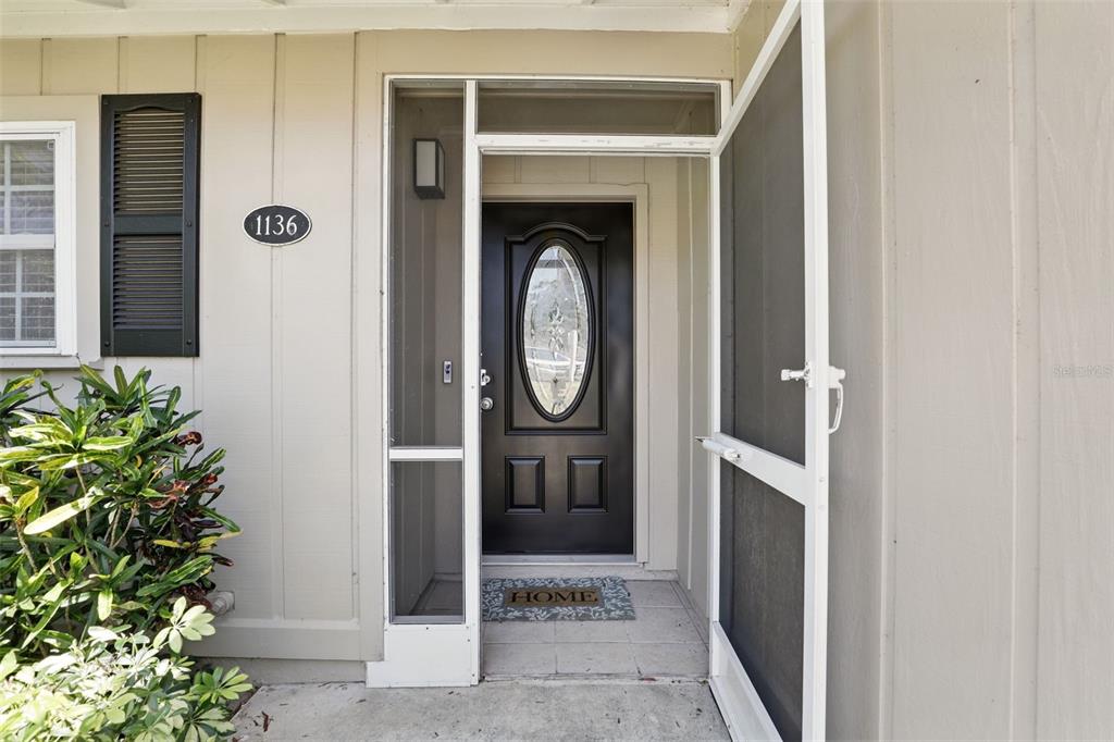 A black front door with an oval glass insert is framed by a white screen door — 1136 VILLA LANE UNIT 96, APOPKA, FL