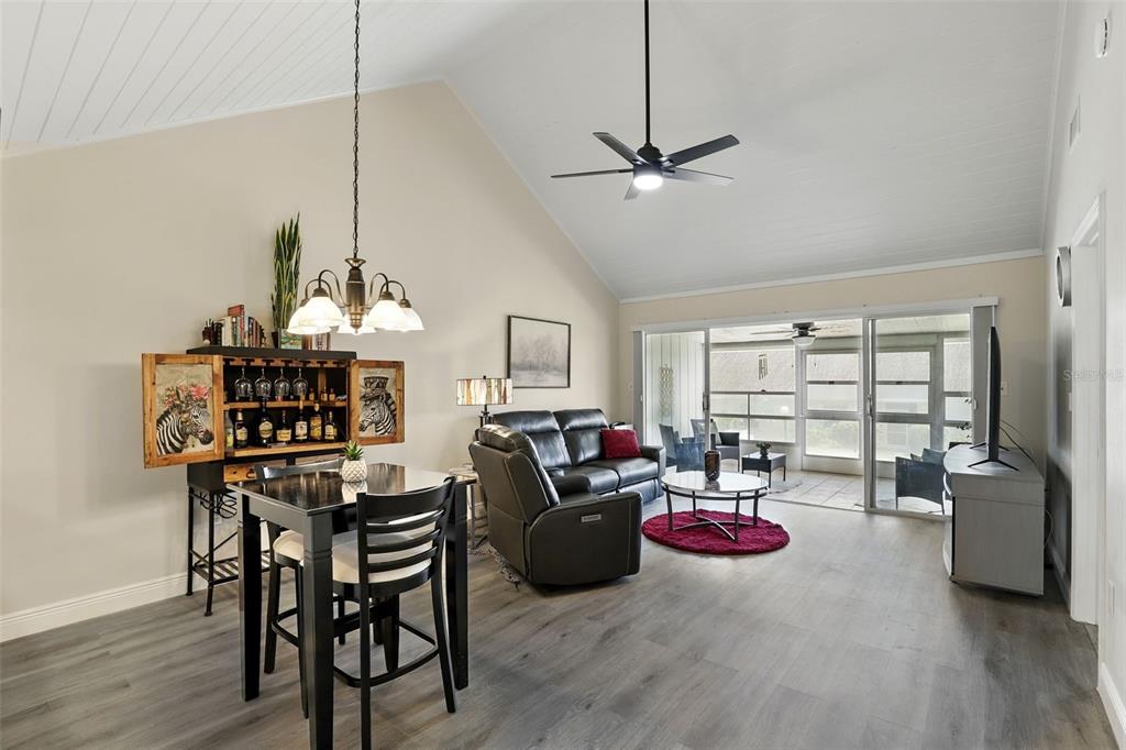 A living and dining area with vaulted ceilings, gray wood flooring, and a sliding glass door — 1136 VILLA LANE UNIT 96, APOPKA, FL