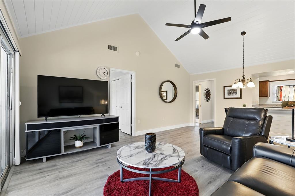 A living room features vaulted ceilings, light wood-look flooring, a television console, and leather furniture — 1136 VILLA LANE UNIT 96, APOPKA, FL