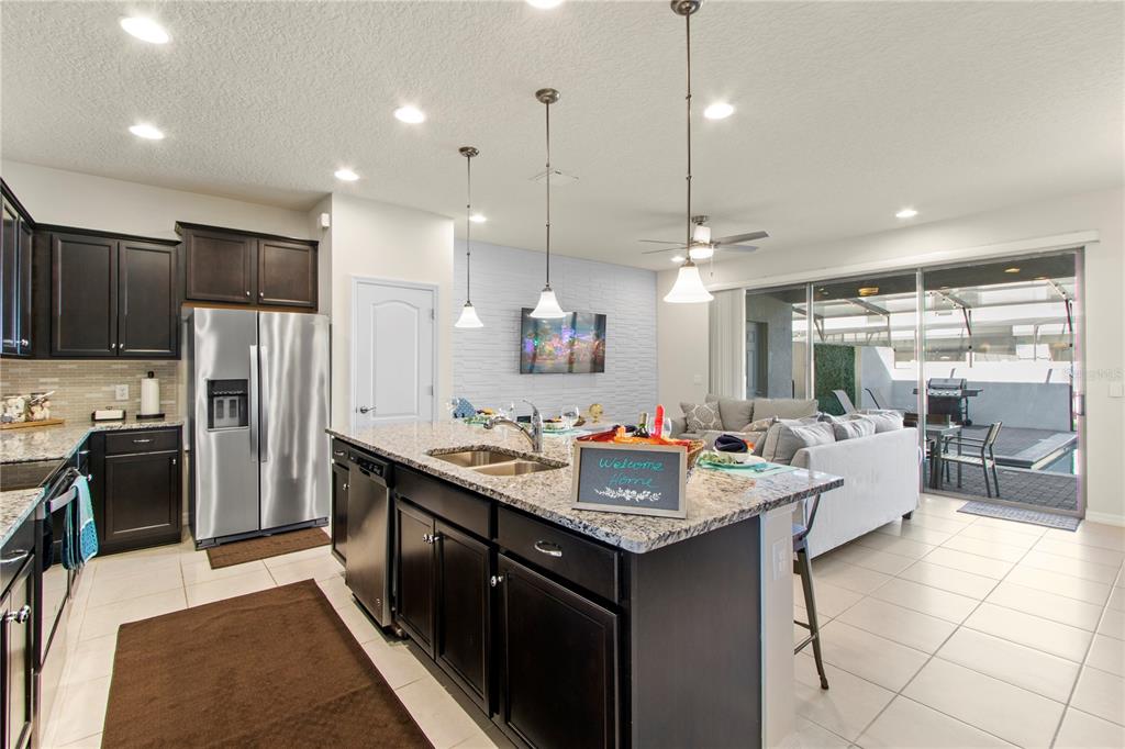 A kitchen with dark cabinets and granite countertops opens to a living area with patio access — 2426 TANGIER DRIVE, KISSIMMEE, FL