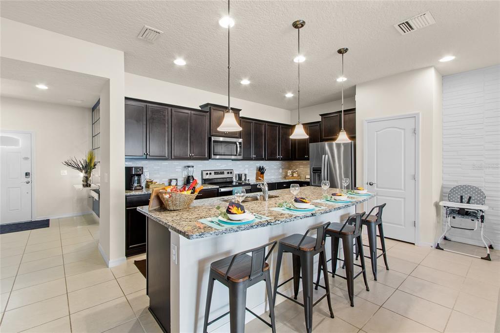 A kitchen features dark wood cabinets, granite countertops, a large island, and three bar stools — 2426 TANGIER DRIVE, KISSIMMEE, FL