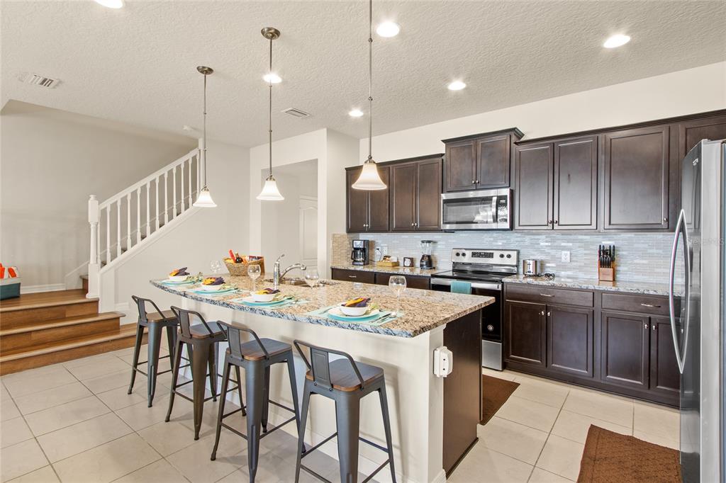 A kitchen with dark wood cabinets, granite countertops, a breakfast bar, and tile flooring — 2426 TANGIER DRIVE, KISSIMMEE, FL