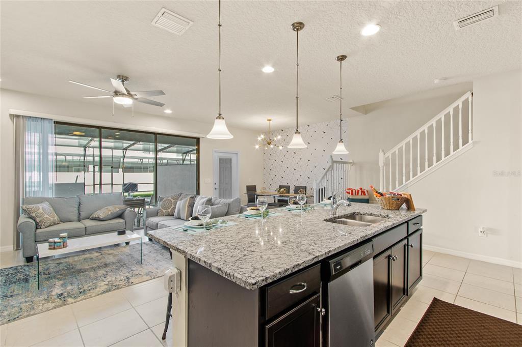 An open-concept kitchen with a granite island overlooks a living room and dining area — 2426 TANGIER DRIVE, KISSIMMEE, FL