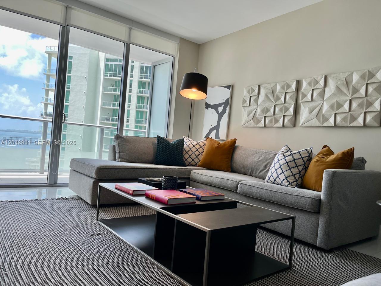 A modern living room features a grey sectional sofa, a coffee table, and balcony views — 1300 Brickell Bay Dr # 2208, Miami FL 33131, MIAMI, FL
