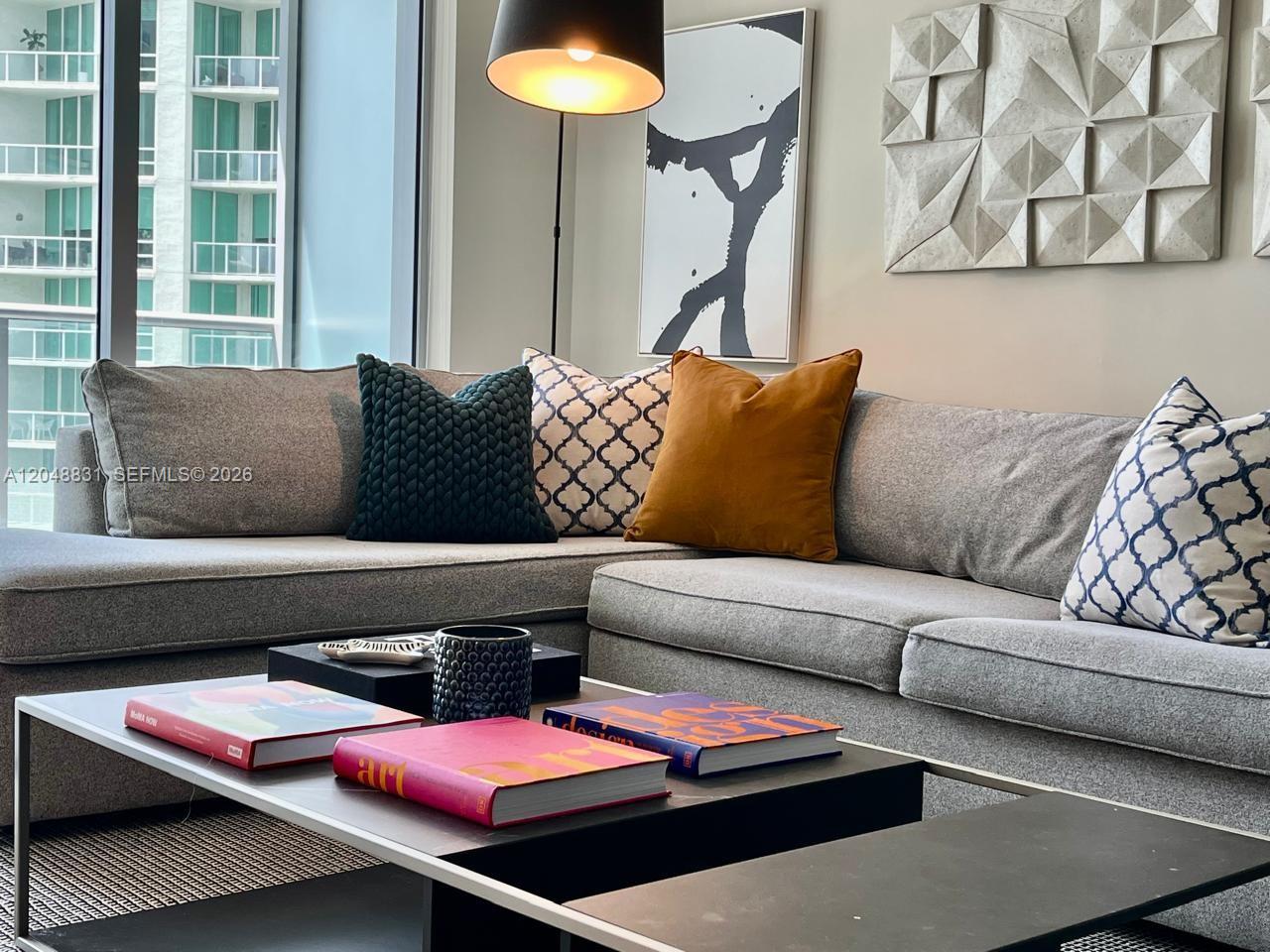 A modern living room features a gray sectional sofa, a coffee table with books, and wall art — 1300 Brickell Bay Dr # 2208, Miami FL 33131, MIAMI, FL