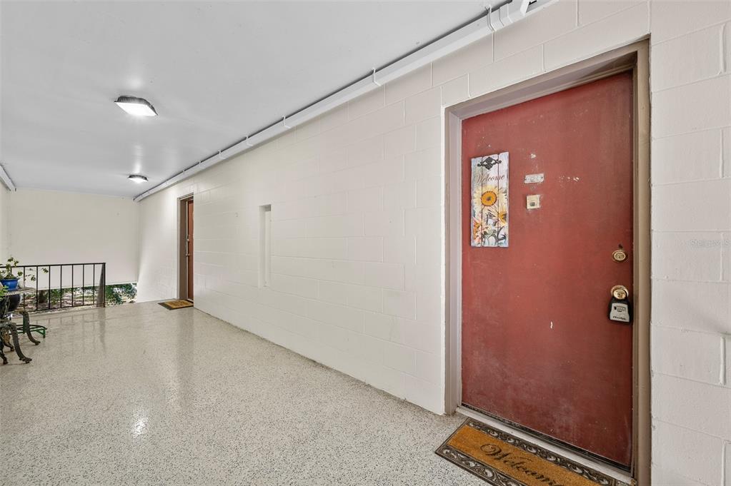 An outdoor walkway with a red door, light-colored block walls, and speckled flooring — 1700 SW 16TH COURT UNIT D24, GAINESVILLE, FL