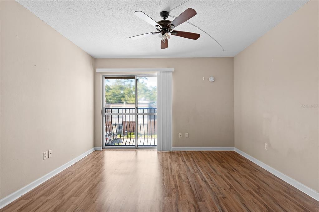 An empty room with wood-look flooring, a ceiling fan, and a sliding glass balcony door — 1700 SW 16TH COURT UNIT D24, GAINESVILLE, FL