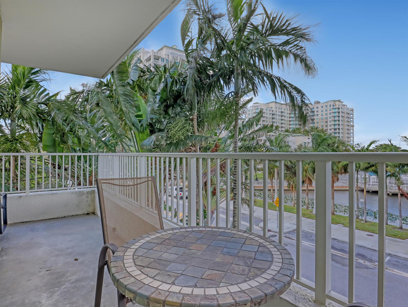 A balcony features a tiled bistro table and chair overlooking palm trees and a waterway — 700 E Boynton Beach Boulevard # 312, Boynton Beach FL 33435, BOYNTON BEACH, FL