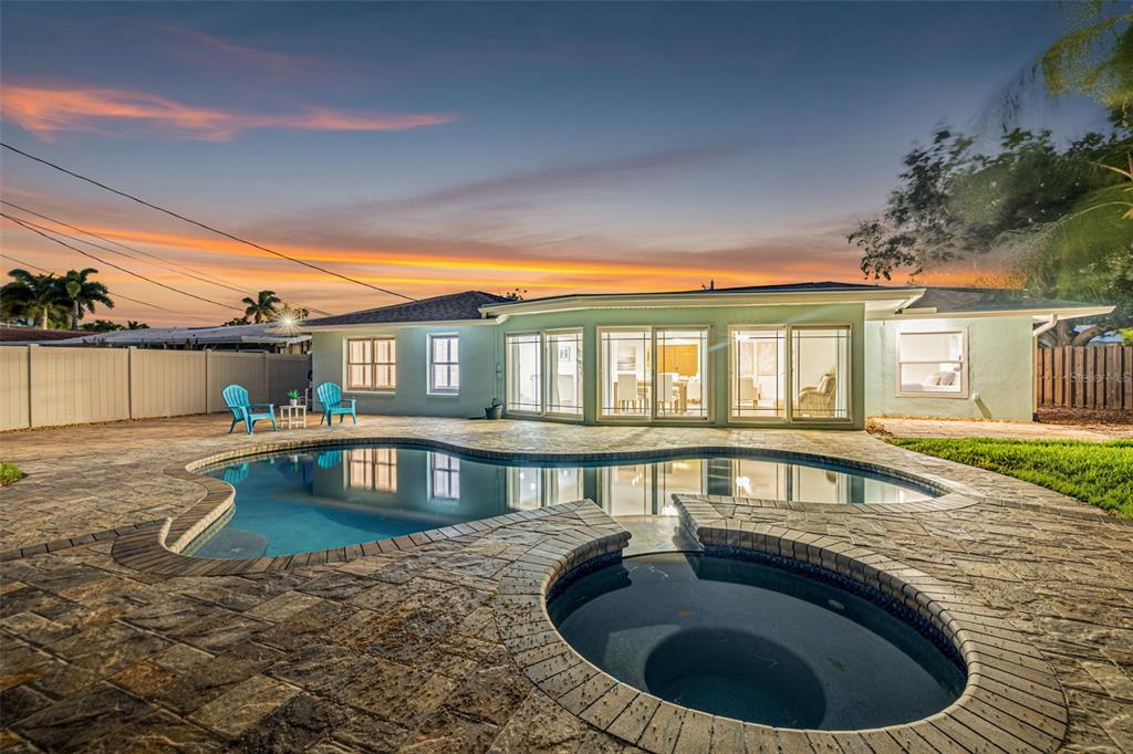 A backyard features a swimming pool, a circular hot tub, and a patio behind a house — 1022 EDEN ISLE DRIVE NE, ST PETERSBURG, FL