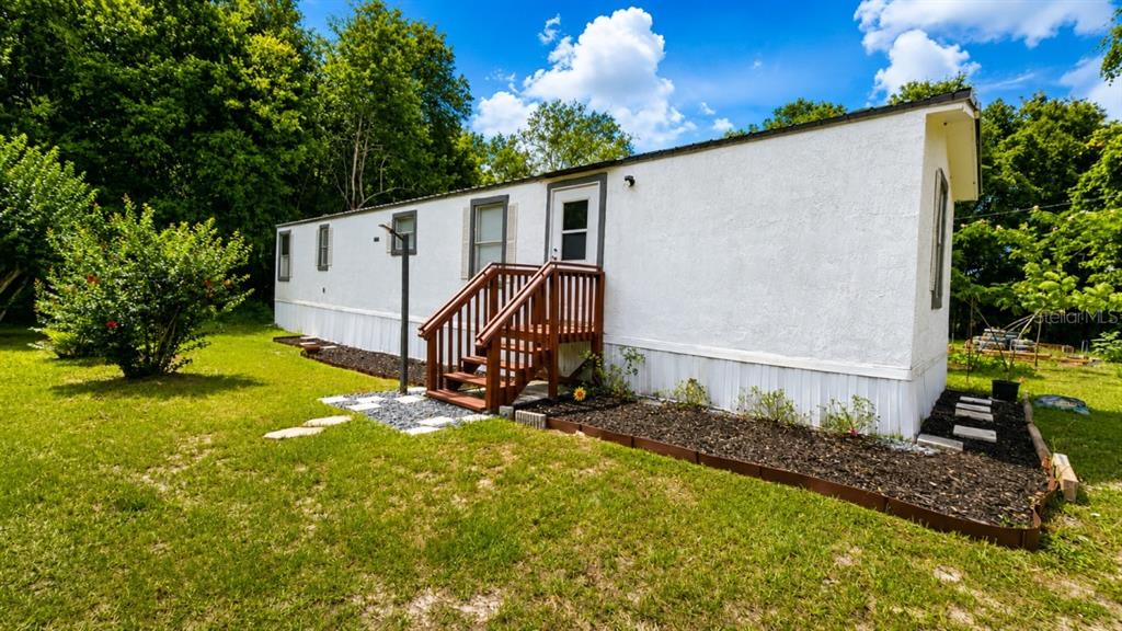A white mobile home features a wooden staircase leading to the entrance door — 24325 SW 46TH AVENUE, NEWBERRY, FL