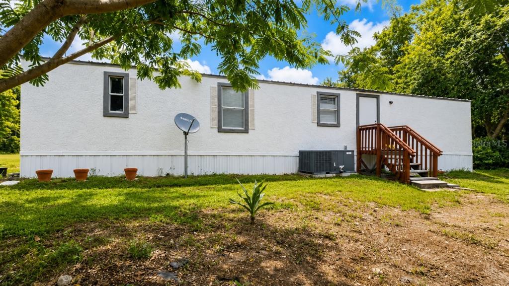 A white mobile home with a wooden staircase, a satellite dish, and three potted plants — 24325 SW 46TH AVENUE, NEWBERRY, FL