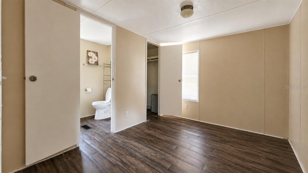 A bedroom with wood-look flooring, beige walls, an attached bathroom, and a closet — 24325 SW 46TH AVENUE, NEWBERRY, FL