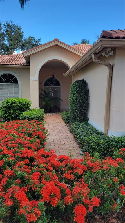 A brick walkway leads to the arched entryway of a house with red roof tiles — 7557 FAIRLINKS COURT, SARASOTA, FL